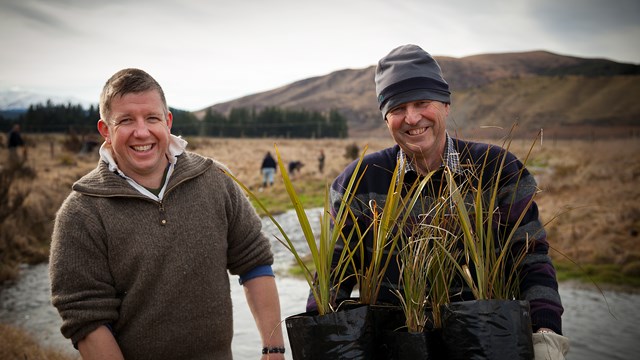 Two farmers holding plants in front of waterway
